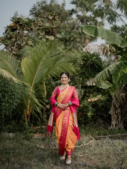 A full-length portrait of a beautiful Maharashtrian bride standing in a lush, tropical setting.