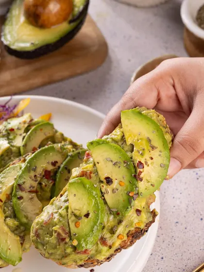 A lifestyle shot of a hand grabbing a slice of avocado toast, making this popular breakfast item look extra appealing.