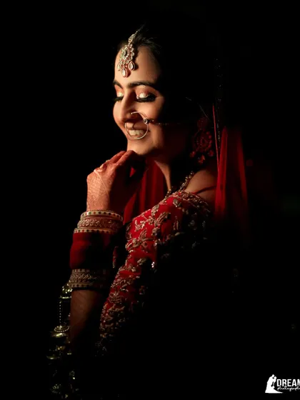 A dramatic low-light portrait of a bride in red, her face gently illuminated, creating a sense of quiet joy.