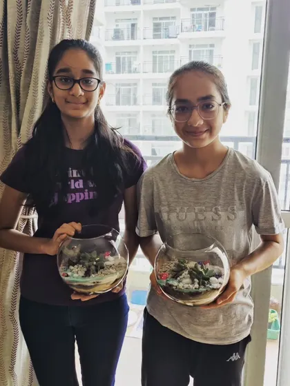 Two sisters proudly holding the beautiful terrariums they created at a workshop. This is a great activity for siblings and friends to do together.