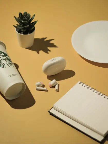 A lifestyle flatlay with realme earbuds, a Starbucks cup, and a notebook, creating a scene of a productive day out.