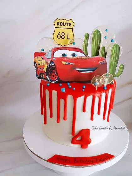 A vibrant Lightning McQueen car themed cake for a 4th birthday. The red drip and desert cactus toppers bring the world of 'Cars' to life.