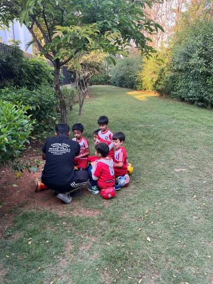 A small group of players sits on their footballs, listening attentively to their coach. This demonstrates the respect and focus we cultivate in our sessions.