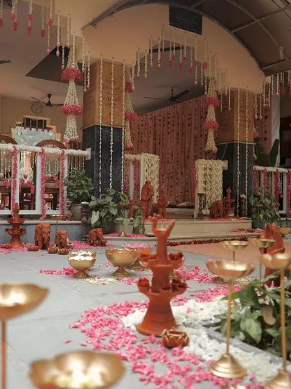 A wide view of a traditional ceremony space we designed. The floor is decorated with scattered flower petals, and the area is filled with terracotta decor, brass urlis, and hanging floral arrangements.