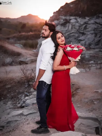 A classic pre-wedding portrait with a vintage feel. The couple posed against a rocky landscape at sunset creates a moody and romantic atmosphere, highlighting the drama and beauty of their love story.