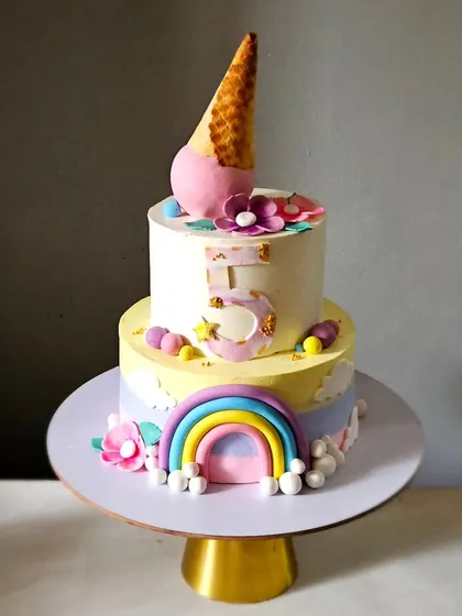 A fun cake combining candy and rainbow themes. This two-tier cake is topped with an ice cream cone and decorated with a pastel rainbow.