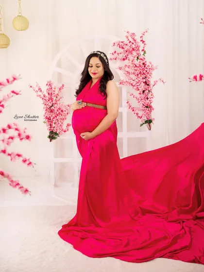A pretty mom-to-be in a vibrant pink gown with a long, flowing train, set against a bright backdrop with cherry blossoms.