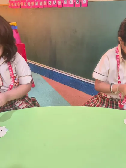 Two girls work on assembling their Grandparents Day cards, carefully gluing the pieces together.