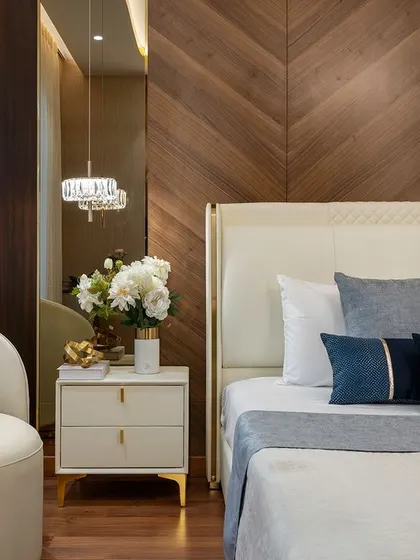 This bedroom exudes warmth and luxury. We designed a chevron-patterned wood accent wall as a backdrop for the cream leather headboard. A curved armchair and pillows in shades of blue add a soft contrast, while a crystal pendant light provides a touch of glamour.