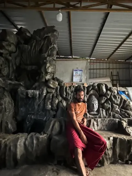 A moment of rest during the creation of a large, custom waterfall installation featuring a Buddha head. This project, combining sculpture and water elements, is a work in progress.