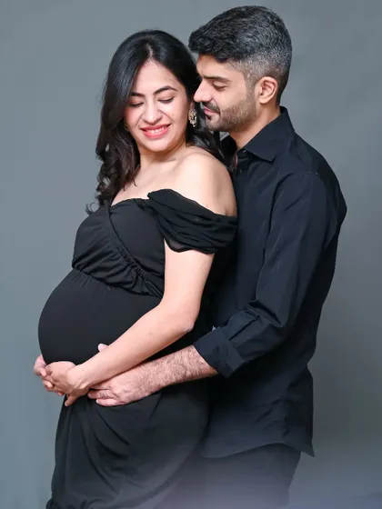 A classic and elegant studio maternity portrait. The couple dressed in all black against a simple grey background creates a sophisticated and timeless look that focuses on emotion.