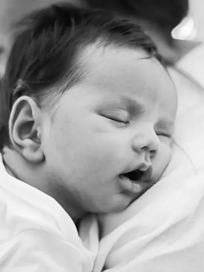 A close-up, black and white shot of a sleeping newborn, safe and sound on their parent's shoulder. This image evokes a feeling of peace and security.