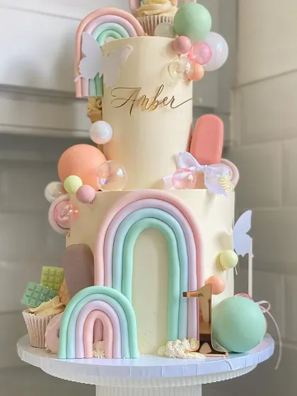 A sweet two-tiered rainbow cake for Amber's first birthday. This "Sweet One" themed cake is loaded with candy, ice cream, and other fun decorations.