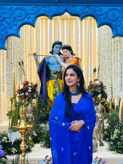 Posing in a simple blue saree at a wedding with a stunning Radha-Krishna decor setup. This shows my work as an influencer and guest at real weddings.
