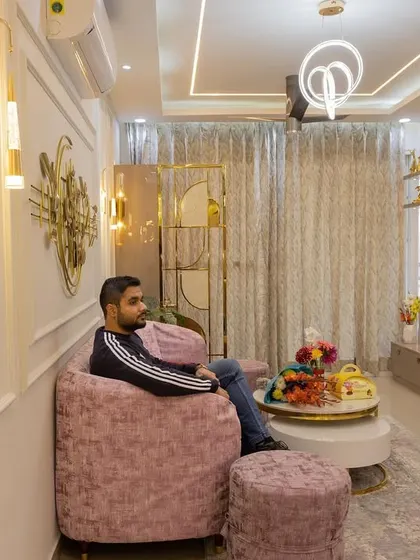 Relaxing in an inviting living room we designed. The space features a plush pink sofa, elegant wall molding with golden accents, and a modern TV unit, creating a perfect blend of comfort and luxury.