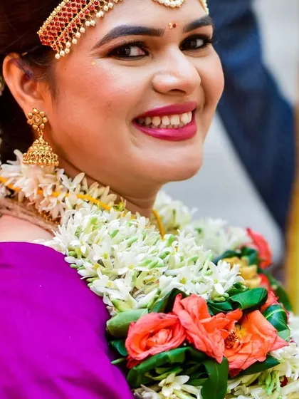 A candid, joyful close-up of a bride during her wedding ceremony, her smile framed by a beautiful floral garland.