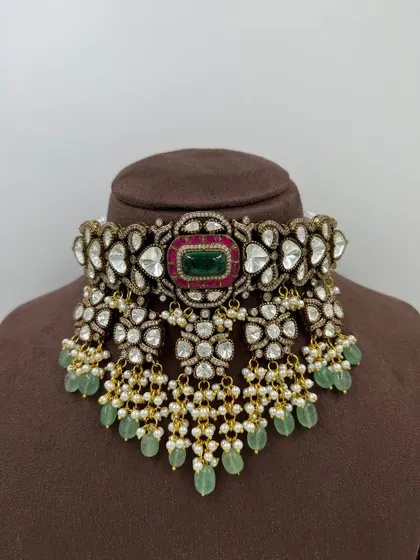 This is a prime example of our grand bridal choker collection. The piece features intricate work with high-quality Kundan, a central emerald-green stone, and delicate pearl and bead droppings, designed to be a showstopper.