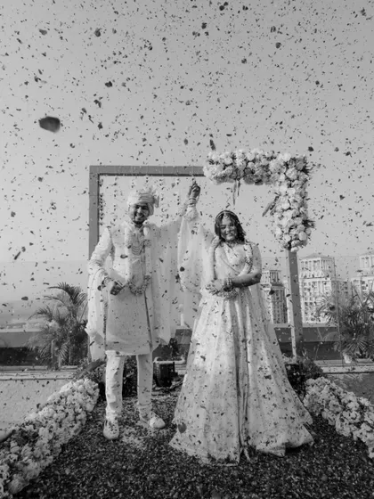The newly married couple stands proudly under a shower of petals in this classic black and white wedding portrait.