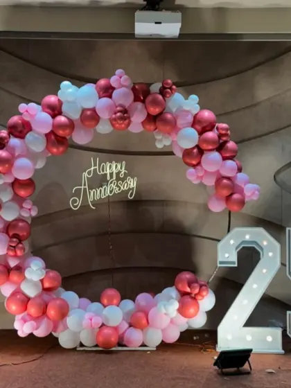 A circular balloon arch in shades of pink and white for a 25th-anniversary party, complete with marquee numbers.