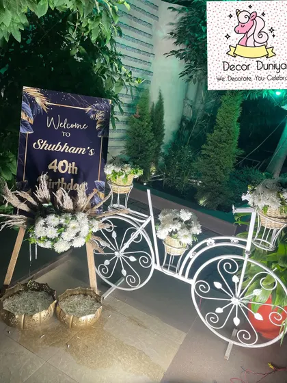 A rustic and chic welcome setup for a 40th birthday, featuring a decorative white bicycle, pampas grass, and a custom welcome sign.