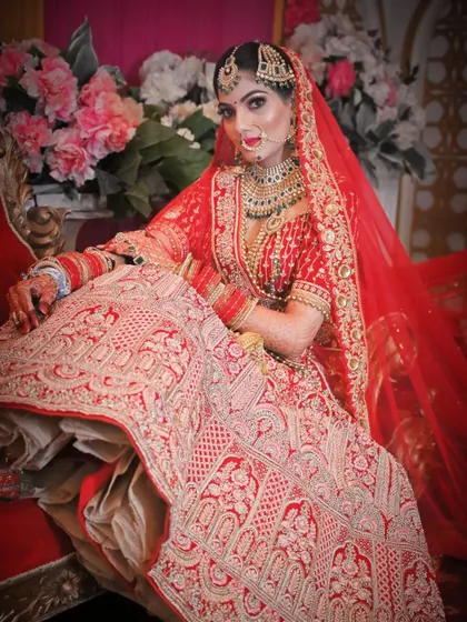 A regal bridal portrait, with the bride seated gracefully, her red and gold lehenga spread out beautifully.