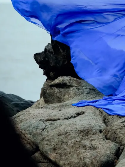 An abstract shot of the blue gown's trail against beach rocks.