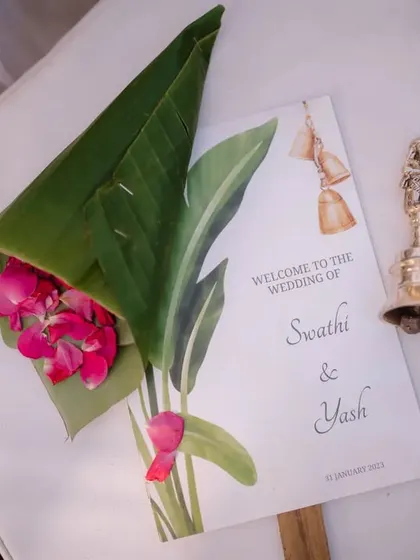 A personalized welcome fan for guests at a traditional South Indian wedding, complete with a small bell for blessings.