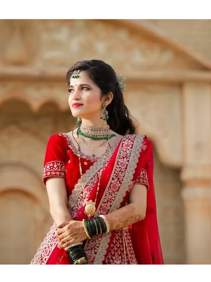 A beautiful portrait of the bride in her red lehenga, looking away thoughtfully. The soft, natural light enhances her features and the details of her attire.