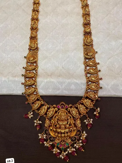 This 92.5 silver gold-plated haram features mango-shaped motifs along the chain and a central Lakshmi pendant. It is a classic piece of South Indian temple jewellery.