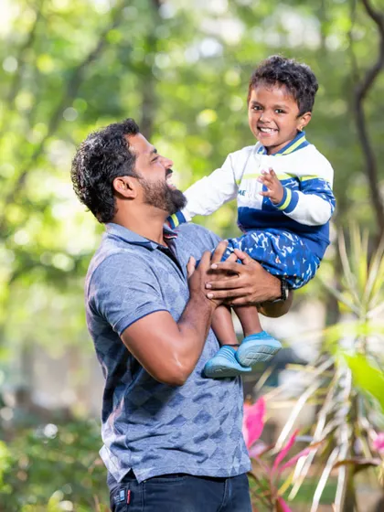 A father lifts his son up, both sharing a moment of pure joy and laughter. This candid outdoor shot perfectly captures the special bond between a dad and his child.