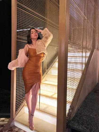 A dramatic pose on a lit staircase in a brown bodycon dress and a faux fur jacket.
