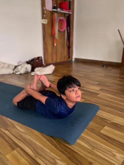 A young boy holds a strong Dhanurasana, or Bow Pose. This backbend is fantastic for strengthening the back muscles and opening the chest.