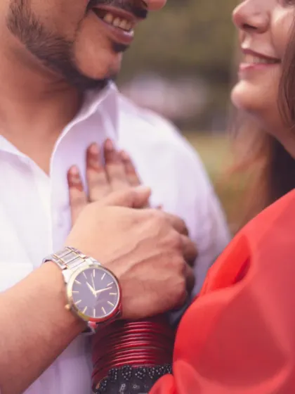 A close-up, intimate shot focusing on the details: the groom's watch, the bride's bangles, and their gentle touch.