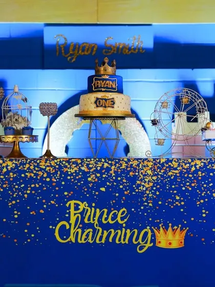 The dessert table for Prince Ryan's royal celebration. The deep blue and gold color scheme, complete with a sparkling "Prince Charming" sign and a crowned cake, creates a look of pure elegance.