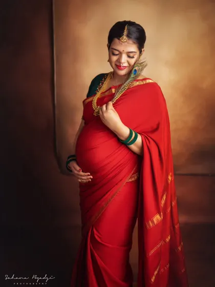 There is a unique power and grace in a traditional maternity portrait. This mom-to-be looks absolutely regal in a classic red silk saree, adorned with temple jewelry and a peacock feather, celebrating her journey with timeless elegance.