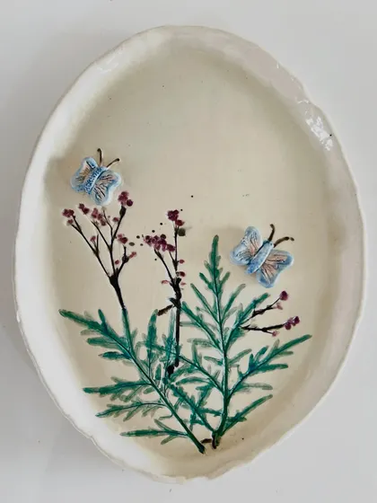 A student's nature-inspired platter, hand-painted with delicate branches and featuring three-dimensional butterflies.