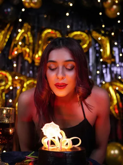 Making a wish. The warm glow from the cake candle, combined with the sparkling gold and black "Happy Birthday" backdrop, creates a magical and intimate moment at an adult birthday party.