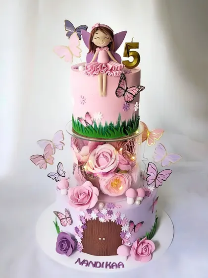 A magical fairy garden cake for a 5th birthday. This tiered cake has a floating middle section filled with flowers and lights, and is decorated with fairies, butterflies, and mushrooms.