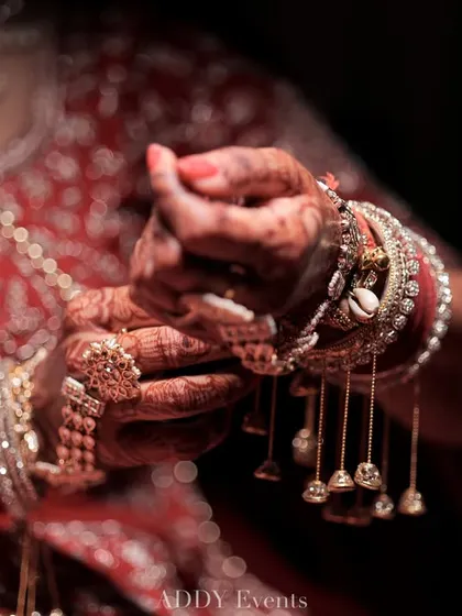 A close-up of the bride's hands, adorned with intricate henna and traditional kalire bangles, a symbol of her new journey.