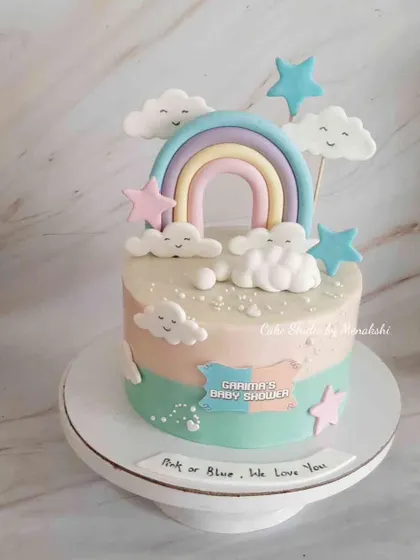 A sweet baby shower cake with a pastel rainbow and smiling clouds. The message 'Pink or Blue, We Love You' makes it perfect for a gender reveal party.