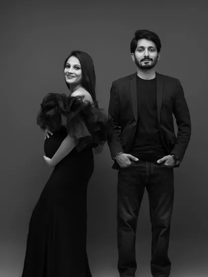 A confident and modern black and white portrait. The couple stands side by side, looking directly at the camera, projecting strength and unity as they embark on their journey to parenthood.