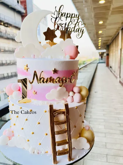 A dreamy two-tier twinkle twinkle little star themed cake. This design features a quilted bottom tier and a pink watercolor top tier with a fondant moon, clouds, and a ladder, perfect for a baby's first birthday.