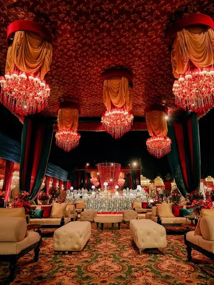 A luxurious lounge area with plush white sofas and cloth-adorned chandeliers. The design uses a rich color palette of red, gold, and teal to create a comfortable yet opulent seating space for guests.