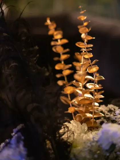 Gilded eucalyptus leaves add a touch of metallic shimmer to the floral arrangements. This detail enhances the luxurious black and gold theme of the event.