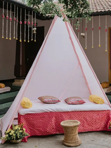 A cozy and chic seating arrangement for the Haldi, featuring a pink teepee-style tent for the couple to relax in.