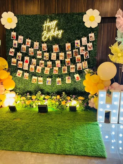 A photo memory wall using an artificial hedge panel as the base. I strung rows of photos for guests to enjoy, and framed the display with balloons, a neon sign, and marquee letters.