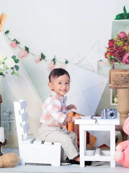 A one-year-old boy looking dapper in a checkered shirt, sitting at a desk in our bright and airy boho-themed setup.