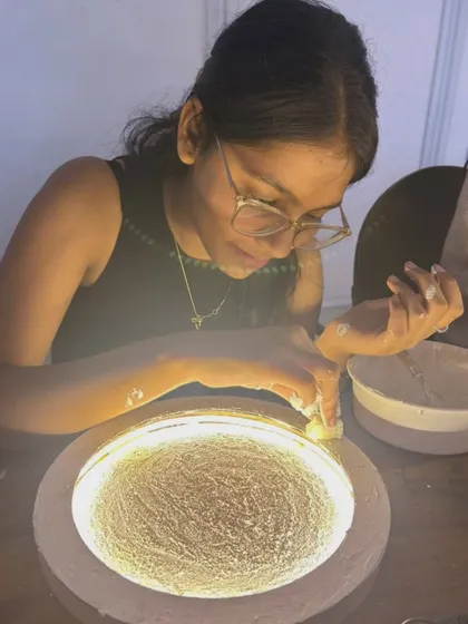 A student carefully applies the finishing touches to her moon lamp, illuminated from within.