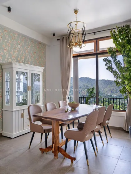 The dining area in 'The Mountain Home,' featuring a solid wood table and comfortable upholstered chairs, all set against a large window with breathtaking views of the valley.
