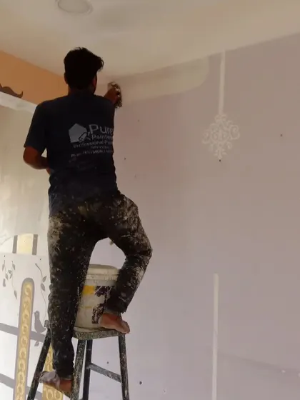 An artist from our team applying a stencil near the ceiling, demonstrating the hands-on, detailed work that goes into our decorative finishes.